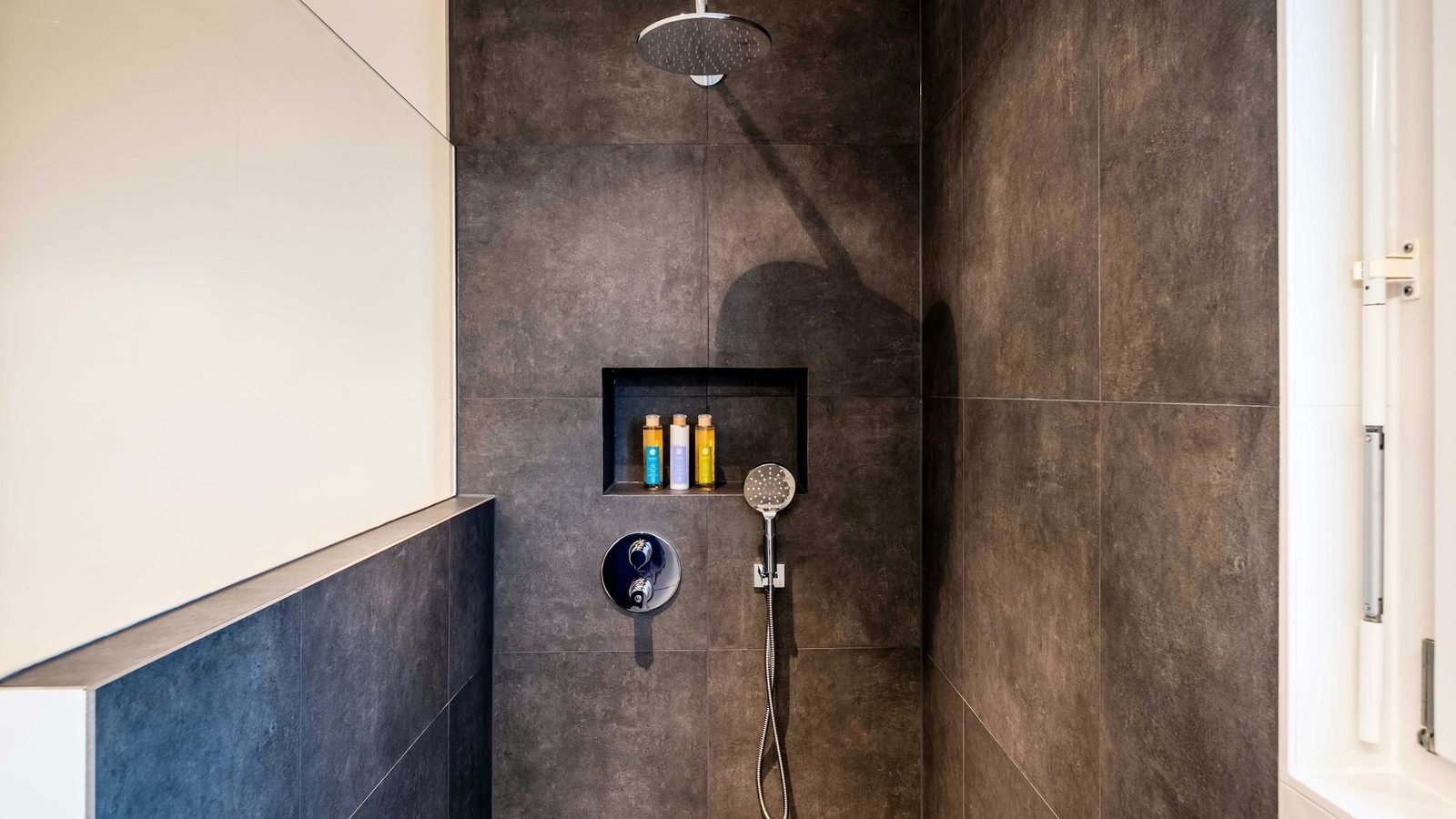 Douche à l'italienne carrelée de grands carreaux sombres, pomme de pluie et niche murale