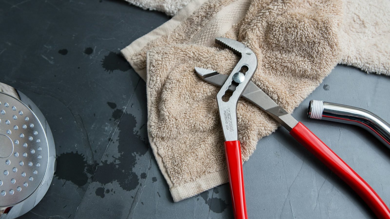 Pince multiprise et douchette posées sur un carrelage gris, chiffon en tissu