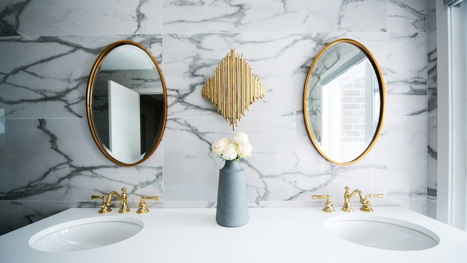 Double vasque sur plan blanc devant un mur en marbre veiné de gris, miroirs et robinets en laiton