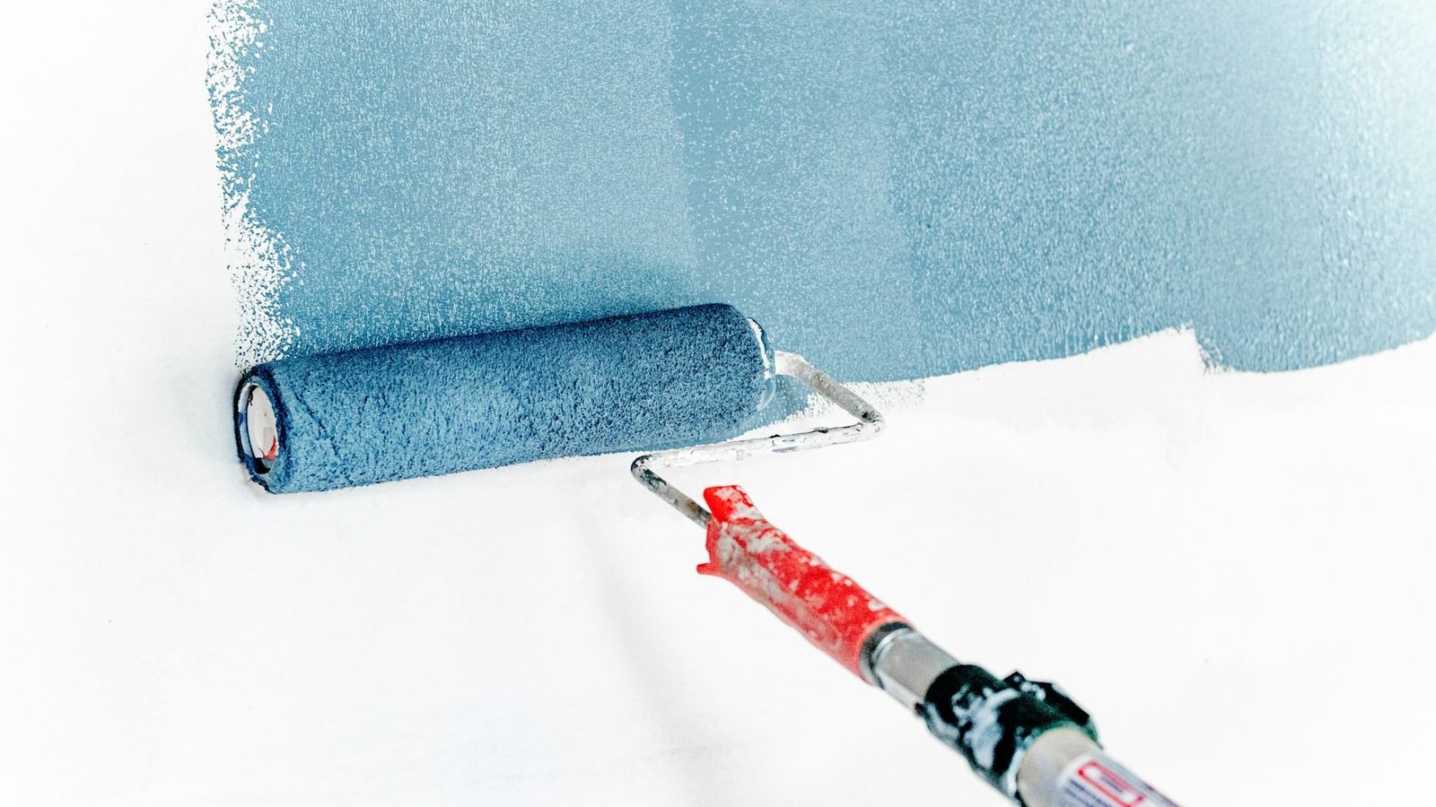 Rouleau chargé de peinture bleu-gris passant sur un mur clair
