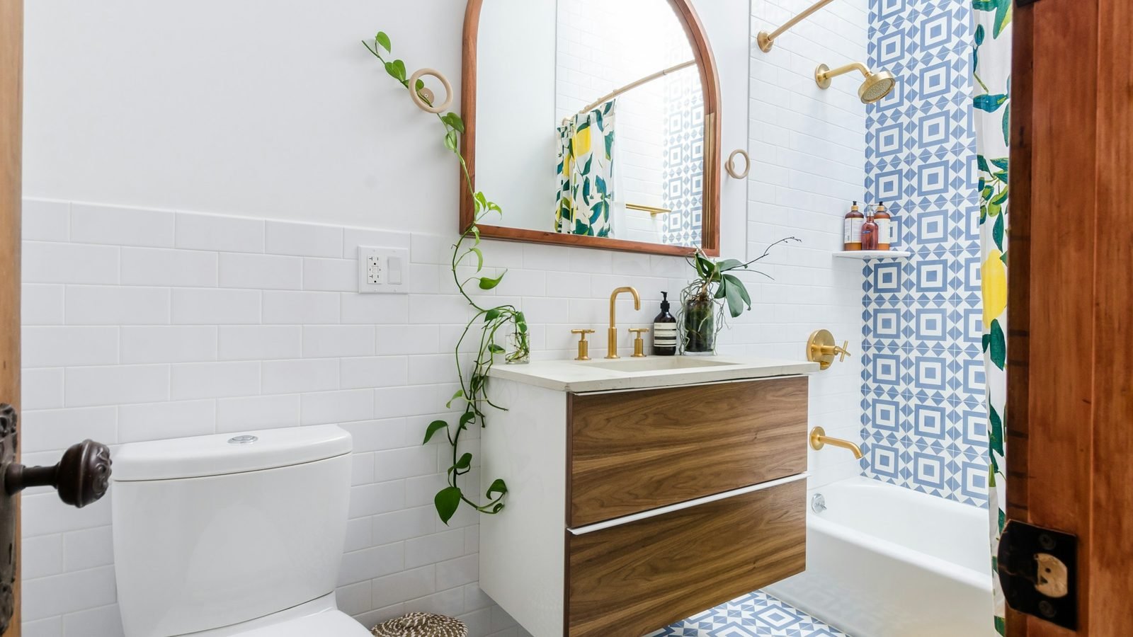Petite salle de bain : meuble suspendu en bois, miroir en arche, plantes, rideau de douche