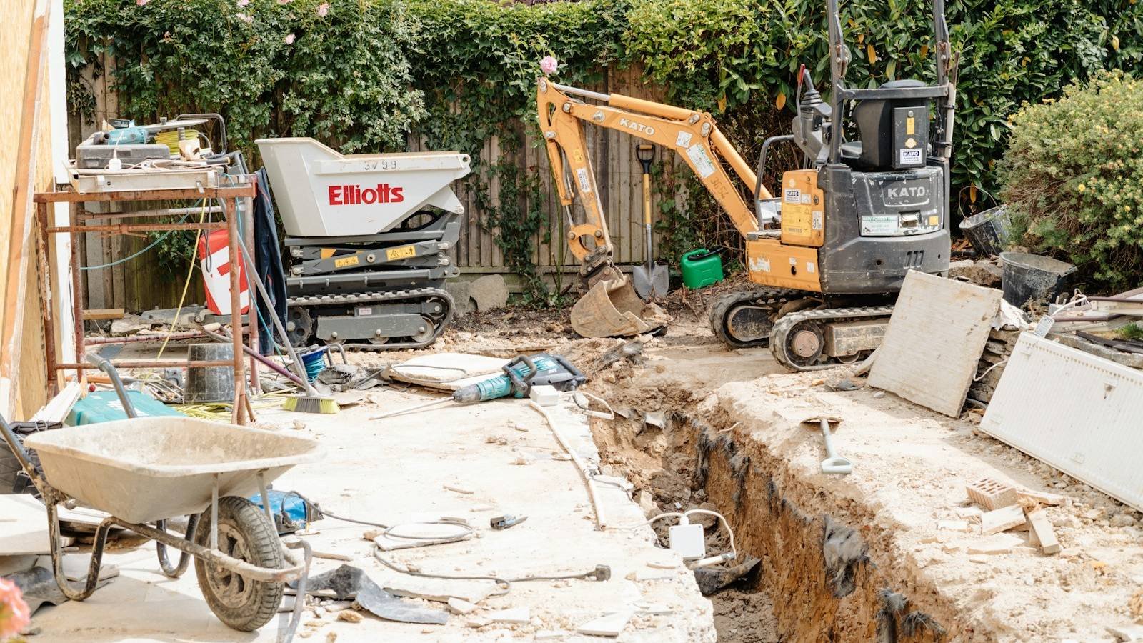 Chantier de piscine dans un jardin : la fouille ouverte, une mini-pelle et une brouette