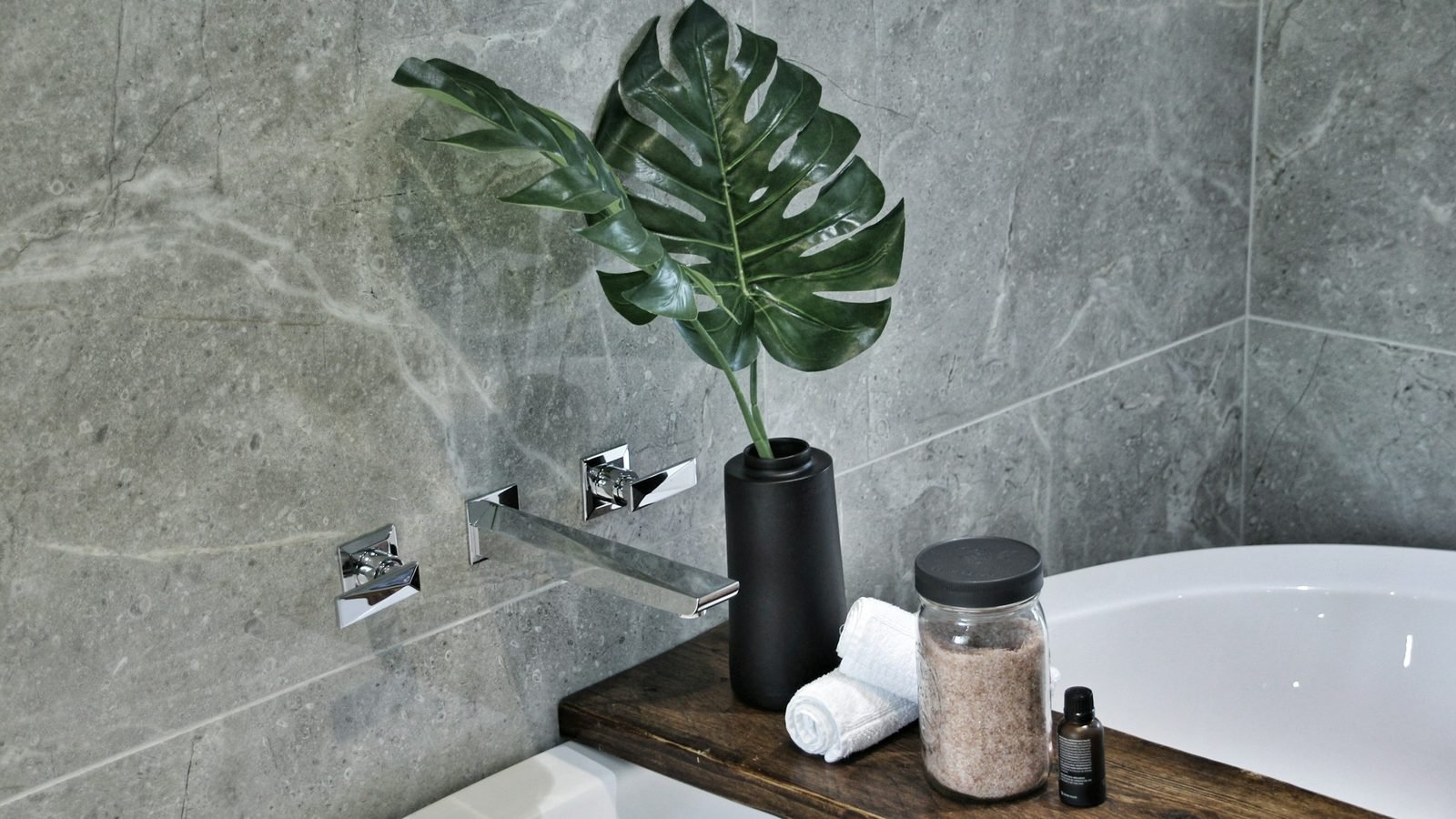 Salle de bain rénovée : mur en pierre grise, tablette en bois, baignoire blanche