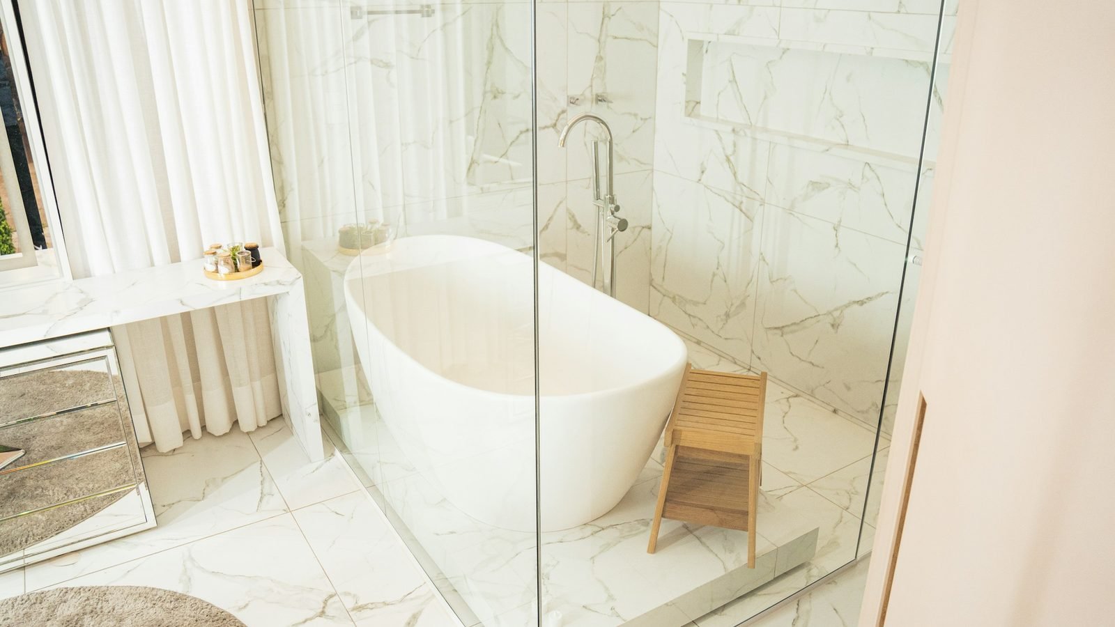 Baignoire îlot à côté d'une douche vitrée dans une salle de bain en marbre clair