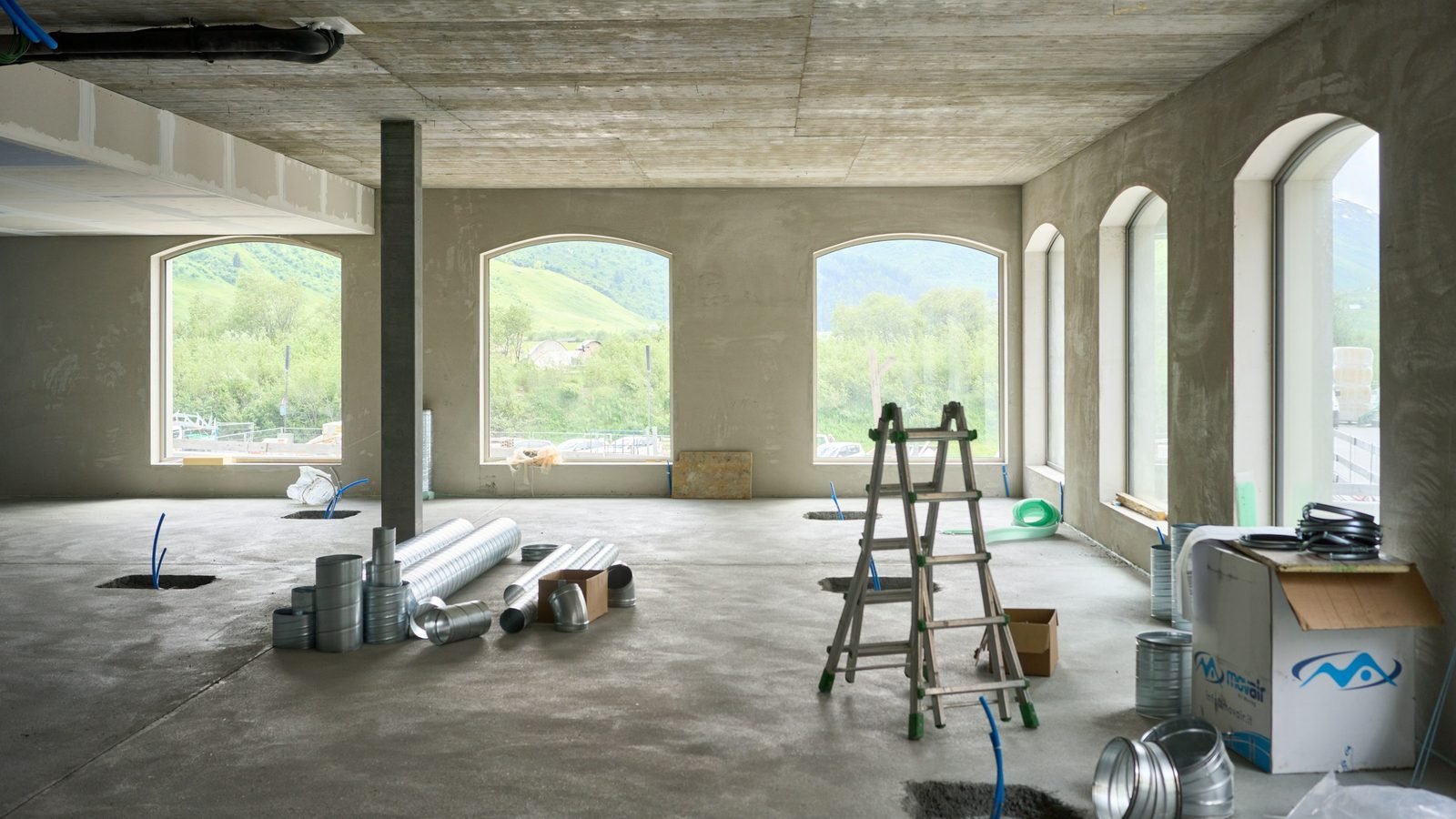 Appartement en plein chantier : échelle double, gaines au sol, grandes fenêtres cintrées