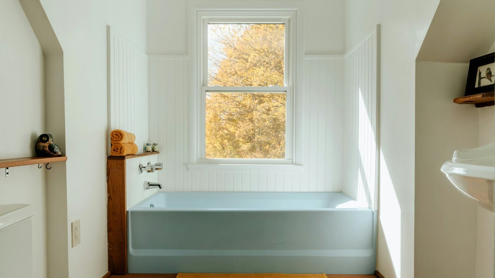 Salle de bain claire avec une fenêtre ouverte sur les arbres au-dessus de la baignoire