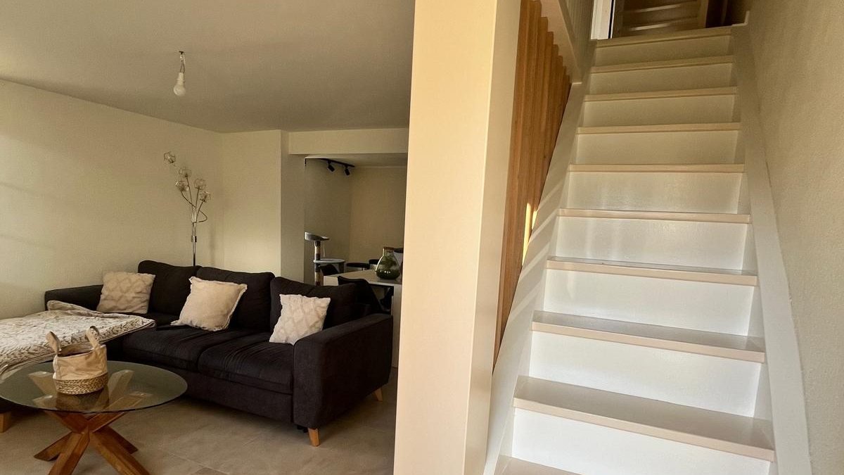 Séjour en fin de chantier : canapé, table basse en verre et escalier blanc à claire-voie en bois
