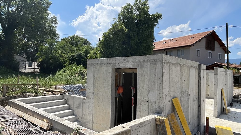 Chantier de gros œuvre : murs en béton fraîchement décoffrés, escalier extérieur, villa en arrière-plan