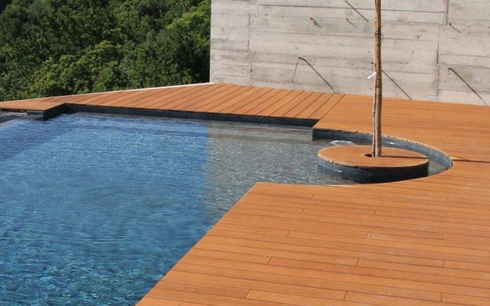 Bord de piscine en lames de bambou brun, mur en béton et arbre planté