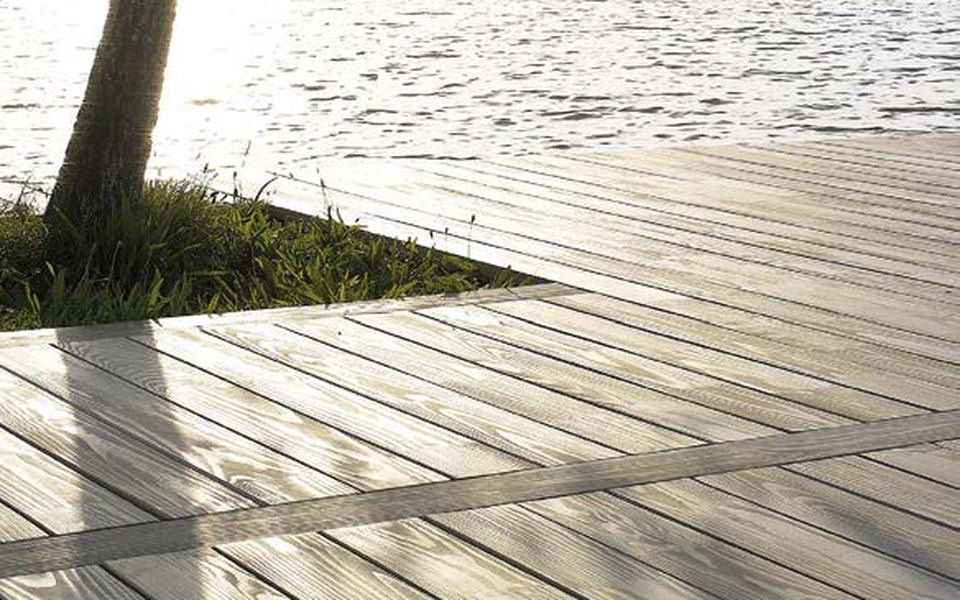 Terrasse en bois gris au bord d'un lac, sous un arbre, à contre-jour