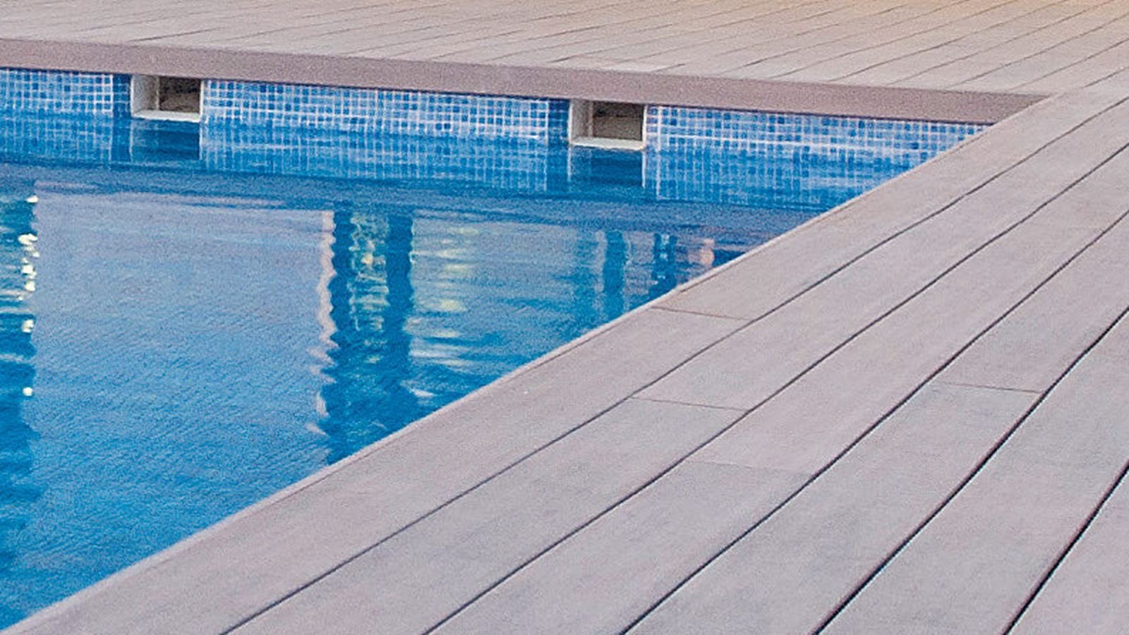 Bord de piscine en lames composite grises, éclairé à la nuit tombée
